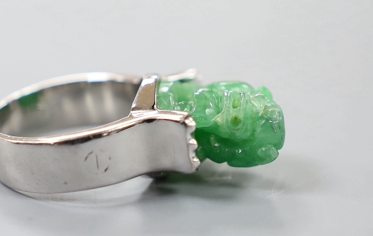 A 585 white metal and jadeite ring, carved with a lion dog, size O, gross weight 11.1 grams.